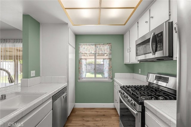 6355 Ortega St, Chino, CA 91710 - kitchen with appliances with stainless steel finishes, tile counters, light wood-type flooring, and white cabinetry