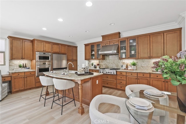 26 Los Indios, Irvine, CA 92618 - kitchen featuring under cabinet range hood, stainless steel appliances, brown cabinetry, a kitchen breakfast bar, and backsplash