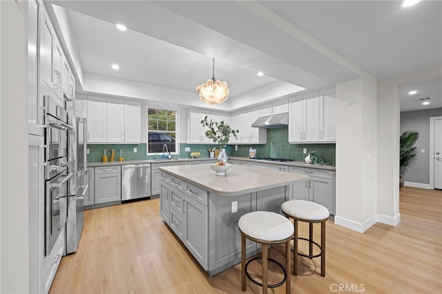 600 Baldwin Ct, Sierra Madre, CA 91024 - kitchen with stainless steel appliances, under cabinet range hood, a raised ceiling, a breakfast bar area, and light wood-type flooring