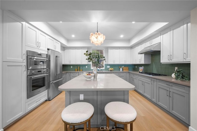 600 Baldwin Ct, Sierra Madre, CA 91024 - kitchen featuring appliances with stainless steel finishes, a tray ceiling, gray cabinetry, under cabinet range hood, and light wood-style flooring