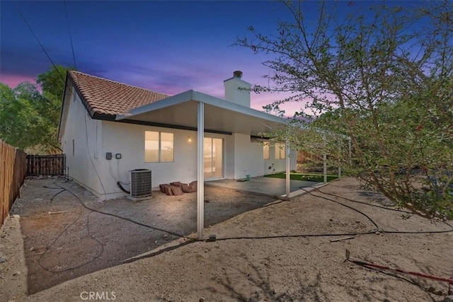 66101 14th St, Desert Hot Springs, CA 92240 - back of property at dusk with a patio, a fenced backyard, a chimney, and stucco siding