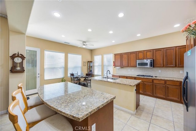 60284 Honeysuckle St, La Quinta, CA 92253 - kitchen featuring a kitchen island with sink, stainless steel microwave, freestanding refrigerator, tasteful backsplash, and a ceiling fan