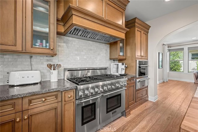 3 Stockmen Rd, Ladera Ranch, CA 92694 - kitchen featuring stainless steel appliances, a warming drawer, custom exhaust hood, brown cabinets, and arched walkways