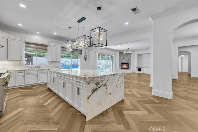 12149 Jonathan Dr, Riverside, CA 92503 - kitchen with arched walkways, white cabinetry, ornamental molding, a chandelier, and an island with sink
