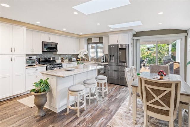 20092 E Frank Ln, Orange, CA 92869 - kitchen with stainless steel appliances, a skylight, white cabinets, light wood-type flooring, and tasteful backsplash