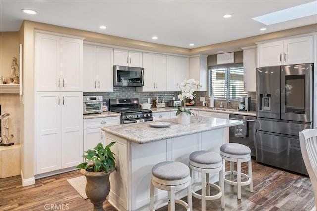 20092 E Frank Ln, Orange, CA 92869 - kitchen featuring appliances with stainless steel finishes, a skylight, wood finished floors, a kitchen island, and white cabinetry