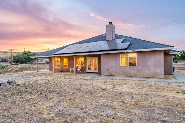 23309 Tak Ct, Tehachapi, CA 93561 - back of house at dusk with french doors, a chimney, roof mounted solar panels, stucco siding, and a patio area