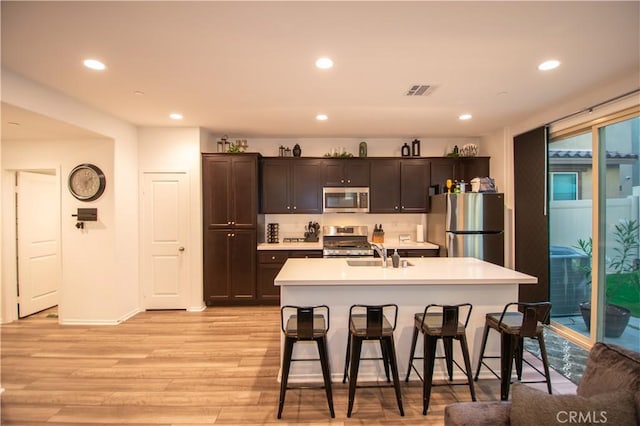 29392 Tourmaline Way, Winchester, CA 92596 - kitchen with appliances with stainless steel finishes, a kitchen bar, light countertops, light wood-style flooring, and recessed lighting