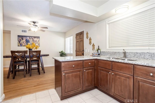 8825 Sophia Ave, North Hills, CA 91343 - kitchen with a peninsula, ceiling fan, light stone countertops, light tile patterned flooring, and brown cabinetry