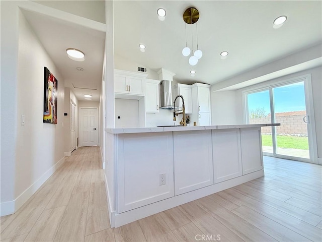 1421 Wildflower St, Rialto, CA 92377 - kitchen with light countertops, white cabinetry, wall chimney exhaust hood, light wood-style flooring, and pendant lighting