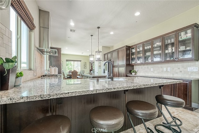6626 W Alluvial Ave, Fresno, CA 93722 - kitchen featuring decorative backsplash, stainless steel gas cooktop, a peninsula, glass insert cabinets, and a kitchen bar