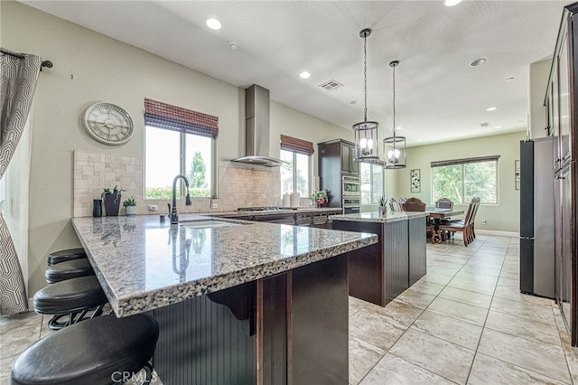 6626 W Alluvial Ave, Fresno, CA 93722 - kitchen featuring wall chimney range hood, a kitchen island, stainless steel appliances, a breakfast bar area, and a peninsula