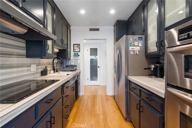 3407 Huxley St Unit 31, Los Angeles, CA 90027 - kitchen featuring extractor fan, stainless steel appliances, light countertops, light wood-style floors, and glass insert cabinets