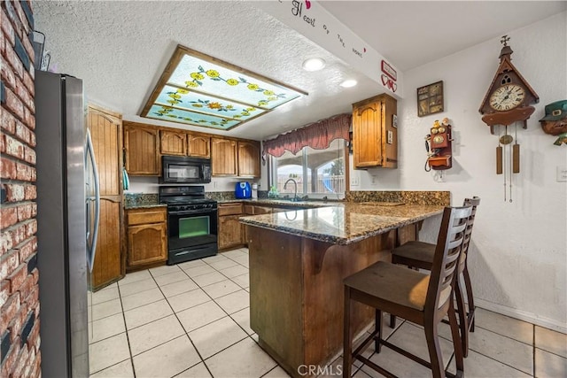 18043 Preston St, Hesperia, CA 92345 - kitchen with black appliances, a peninsula, brown cabinets, light tile patterned flooring, and dark stone countertops