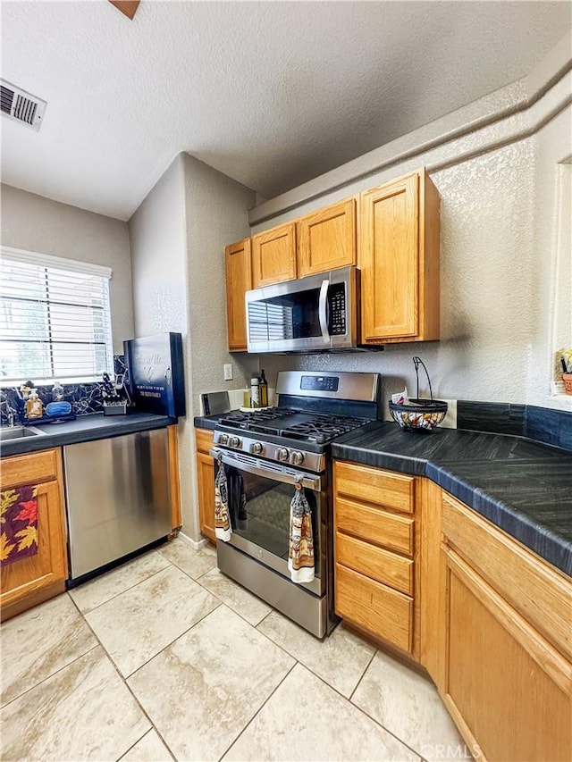 204 Shaded Palm, Blythe, CA 92225 - kitchen featuring stainless steel appliances, dark countertops, a textured wall, a textured ceiling, and light tile patterned floors