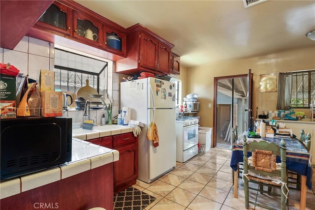 2734 S Redondo Blvd, Los Angeles, CA 90016 - kitchen featuring white appliances, tile counters, reddish brown cabinets, glass insert cabinets, and light tile patterned flooring