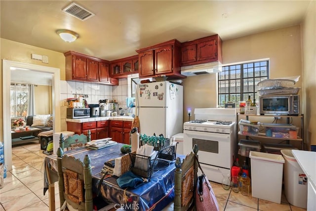 2734 S Redondo Blvd, Los Angeles, CA 90016 - kitchen with white appliances, under cabinet range hood, tile counters, light tile patterned flooring, and decorative backsplash