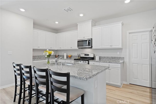 25541 Buckeye Meadow Ln, Homeland, CA 92548 - kitchen with stainless steel appliances, light wood-type flooring, white cabinetry, a breakfast bar, and recessed lighting