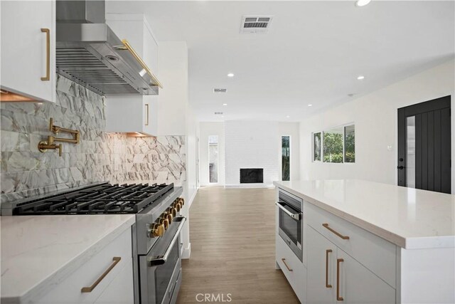 1230 Spazier Ave, Glendale, CA 91201 - kitchen with wall chimney range hood, high end stainless steel range oven, white cabinetry, recessed lighting, and light wood-style flooring
