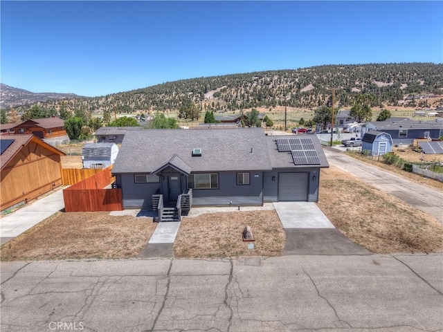 2217 Juniper Ln, Big Bear City, CA 92314 - view of front of house with roof mounted solar panels, roof with shingles, a mountain view, driveway, and a garage