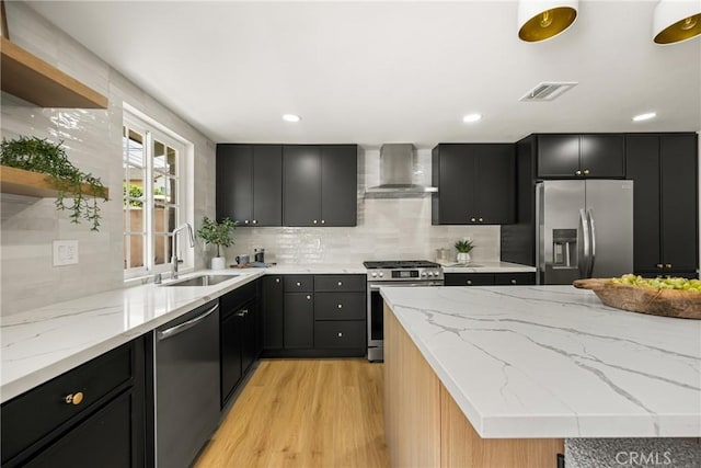 121 W Borromeo Ave, Placentia, CA 92870 - kitchen featuring appliances with stainless steel finishes, wall chimney range hood, dark cabinetry, light wood finished floors, and light stone counters