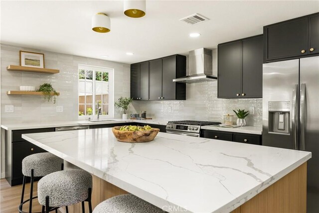 121 W Borromeo Ave, Placentia, CA 92870 - kitchen featuring wall chimney range hood, stainless steel appliances, dark cabinets, tasteful backsplash, and a breakfast bar area