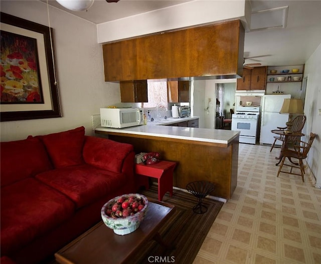 937 E 6th St, Madera, CA 93638 - kitchen featuring white appliances, light floors, a peninsula, under cabinet range hood, and brown cabinets