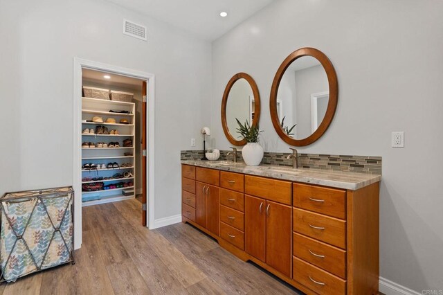 1740 Fire Mountain Dr, Oceanside, CA 92054 - bathroom with double vanity, wood finished floors, a walk in closet, tasteful backsplash, and recessed lighting