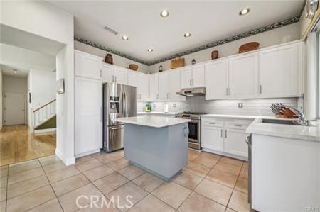 14213 Aliso Ct, Chino Hills, CA 91709 - kitchen with appliances with stainless steel finishes, under cabinet range hood, light tile patterned floors, a kitchen island, and white cabinetry