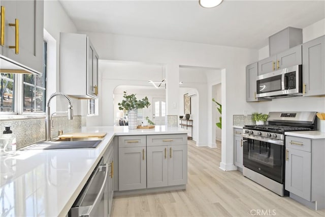 215 E 107th St, Los Angeles, CA 90003 - kitchen featuring stainless steel appliances, gray cabinetry, light wood-style flooring, decorative backsplash, and a peninsula