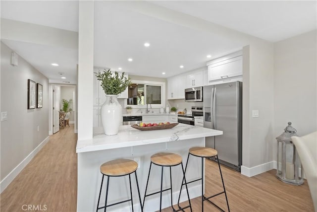 4025 Calle Sonora Este Unit 2C, Laguna Woods, CA 92637 - kitchen featuring stainless steel appliances, a kitchen breakfast bar, light stone counters, white cabinets, and light wood-style flooring