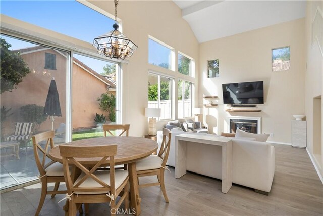 26 Le Vanto, Irvine, CA 92606 - dining area with light wood-style flooring, high vaulted ceiling, a glass covered fireplace, and a chandelier