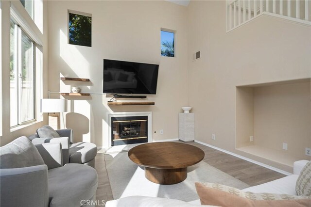 26 Le Vanto, Irvine, CA 92606 - living room featuring healthy amount of natural light, wood finished floors, a towering ceiling, and a glass covered fireplace