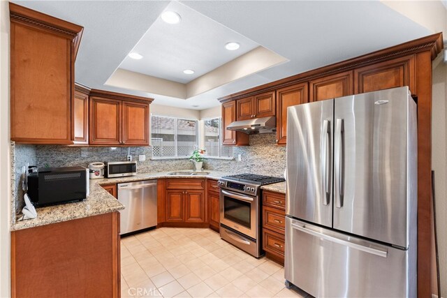 17300 Azalea Ct, La Puente, CA 91744 - kitchen featuring appliances with stainless steel finishes, under cabinet range hood, brown cabinets, a tray ceiling, and recessed lighting