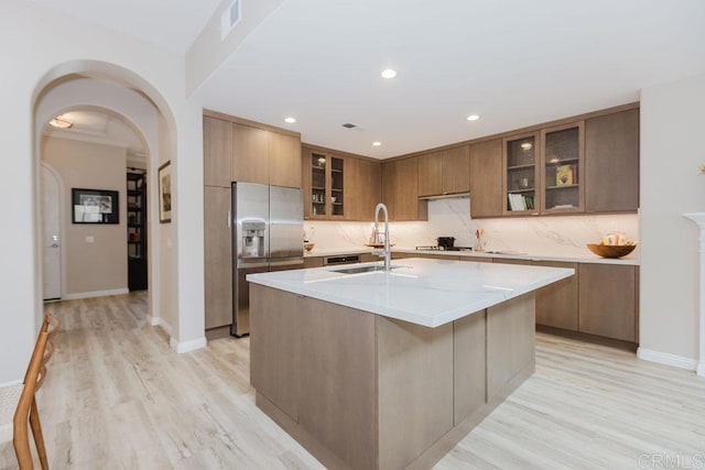 2740 E Bainbridge Rd, San Diego, CA 92106 - kitchen featuring stainless steel fridge with ice dispenser, backsplash, light wood-style floors, arched walkways, and an island with sink