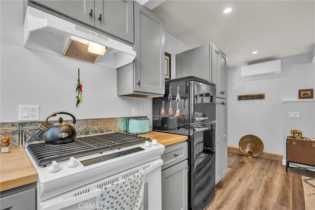 16635 Mountain View Dr, Cobb, CA 95426 - kitchen with under cabinet range hood, white gas range, a wall mounted air conditioner, wooden counters, and gray cabinets