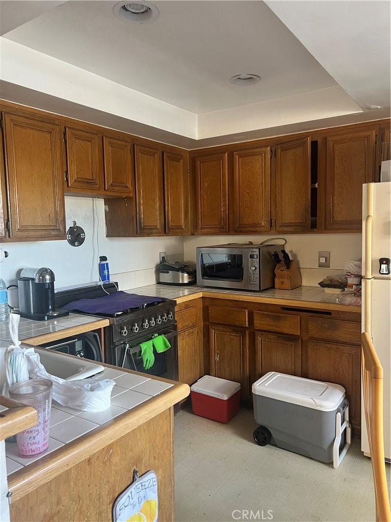 17333 Brookhurst St Unit B7, Fountain Valley, CA 92708 - kitchen featuring stainless steel microwave, tile counters, freestanding refrigerator, high end black range oven, and brown cabinetry