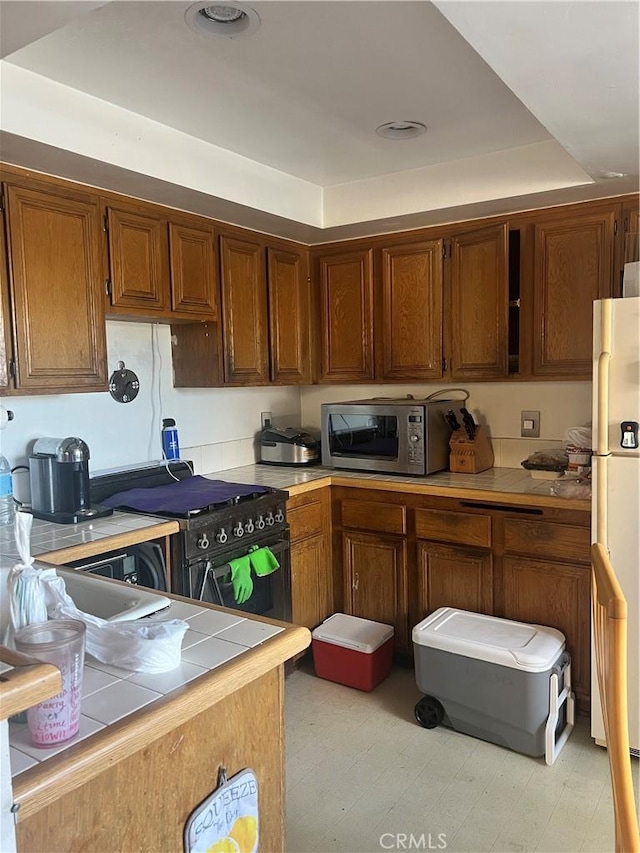 17333 Brookhurst St Unit B7, Fountain Valley, CA 92708 - kitchen featuring stainless steel microwave, tile counters, freestanding refrigerator, high end black range oven, and brown cabinetry