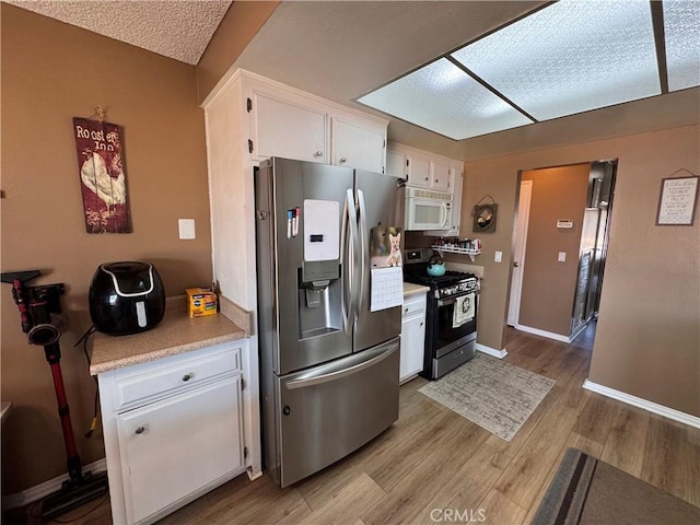 811 Mescal Dr, Barstow, CA 92311 - kitchen featuring appliances with stainless steel finishes, white cabinets, light countertops, light wood-style flooring, and a textured ceiling