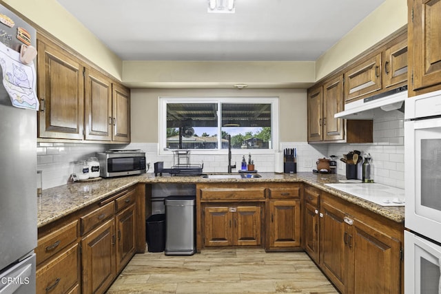 6100 Carter Ave, Bakersfield, CA 93308 - kitchen featuring appliances with stainless steel finishes, decorative backsplash, light wood-style flooring, under cabinet range hood, and stone counters