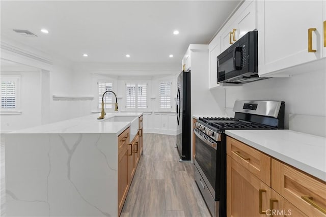 5171 S Wilton Pl, Los Angeles, CA 90062 - kitchen with black appliances, light wood-style floors, an island with sink, light stone counters, and white cabinets