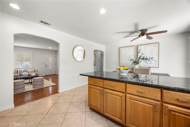 4161 E Fauna Ave, Anaheim, CA 92807 - kitchen with arched walkways, a ceiling fan, light tile patterned floors, dark stone countertops, and brown cabinetry