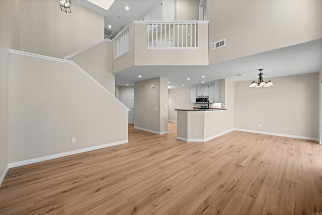 4625 Los Alamos Way Unit C, Oceanside, CA 92057 - unfurnished living room with stairway, a chandelier, light wood-style flooring, a high ceiling, and recessed lighting