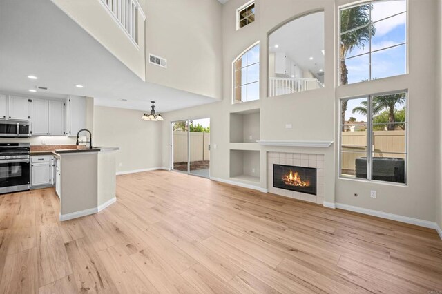 4625 Los Alamos Way Unit C, Oceanside, CA 92057 - unfurnished living room with built in shelves, a chandelier, a fireplace, light wood-style flooring, and a high ceiling
