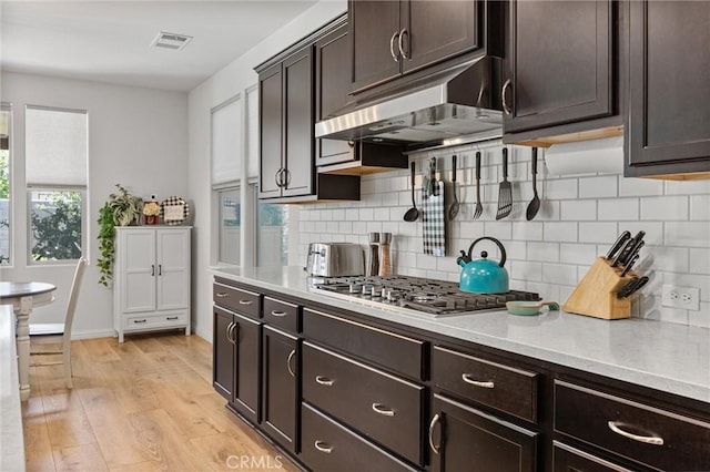 14217 Pemberley Passage Ave, Bakersfield, CA 93311 - kitchen featuring stainless steel gas stovetop, under cabinet range hood, tasteful backsplash, light wood-style flooring, and dark brown cabinets
