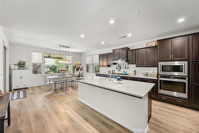 14217 Pemberley Passage Ave, Bakersfield, CA 93311 - kitchen featuring appliances with stainless steel finishes, under cabinet range hood, dark brown cabinetry, an island with sink, and recessed lighting