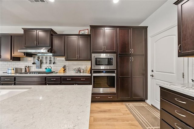 14217 Pemberley Passage Ave, Bakersfield, CA 93311 - kitchen with appliances with stainless steel finishes, under cabinet range hood, dark brown cabinetry, and light wood-style flooring