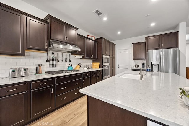 14217 Pemberley Passage Ave, Bakersfield, CA 93311 - kitchen with stainless steel appliances, under cabinet range hood, light wood-style floors, backsplash, and light stone countertops