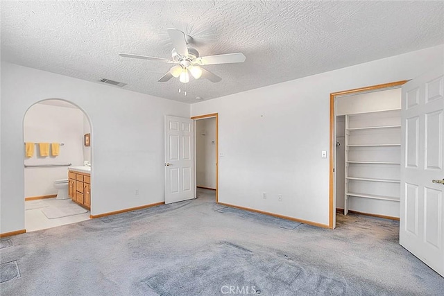 14158 Tu Su Cir, Apple Valley, CA 92307 - unfurnished bedroom featuring a walk in closet, arched walkways, light carpet, ensuite bath, and a ceiling fan