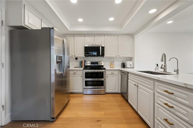 8396 Goldsport Cir, Huntington Beach, CA 92646 - kitchen featuring appliances with stainless steel finishes, a raised ceiling, light wood finished floors, white cabinetry, and recessed lighting